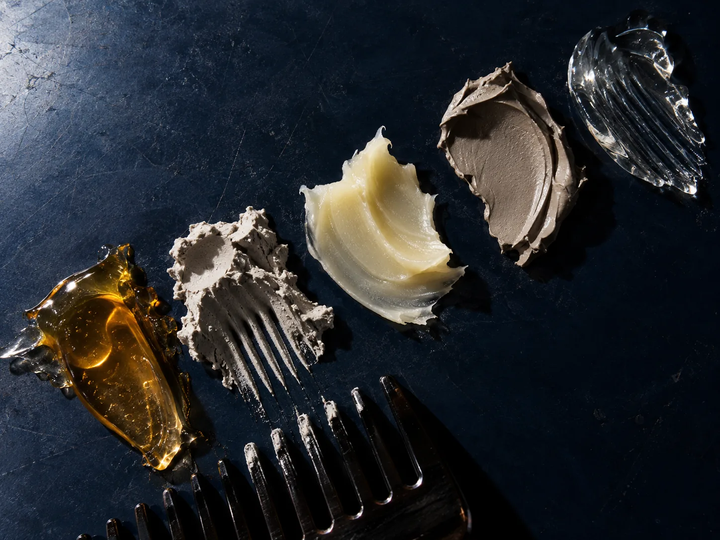 Contrasting styling product textures and comb marks on a dark surface